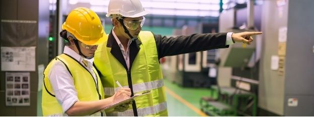 Två personer i skyddsutrustning inspekterar en industrimiljö